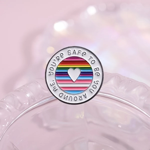 Macro detail of round rainbow enamel pin with 'You're safe to be you around me' text
