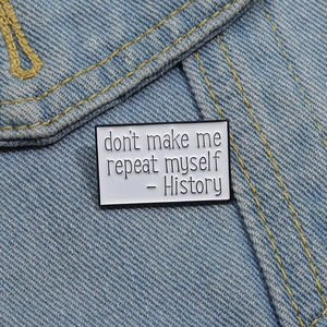 Close-up of a rectangular enamel pin with history quote on blue denim fabric