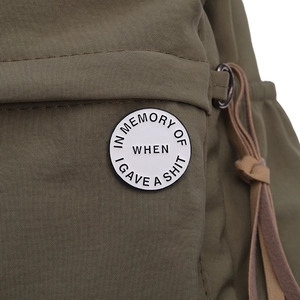 Detail of round white enamel pin badge with funny text on olive green fabric