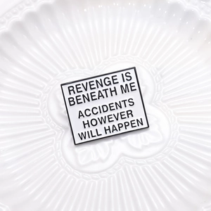 Detail of square enamel pin with text Revenge Is Beneath Me Accidents However Will Happen
