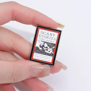 Scary Stories to Tell in the Dark enamel book pin badge held in hand with white background