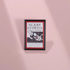 Macro view of book-shaped enamel pin with Scary Stories motif and skull illustration