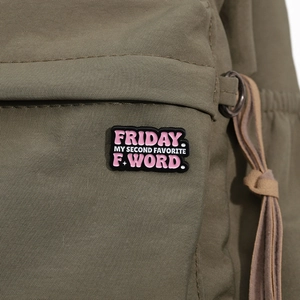 Gros plan du pin's en émail noir avec texte Friday sur tissu en toile verte