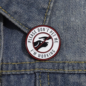 Round metal enamel service dog pin with 'PLEASE DON'T PET ME I'M WORKING' text on denim