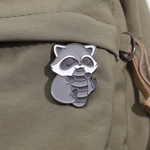 Macro shot of a cute cartoon raccoon enamel pin attached to an olive green canvas bag