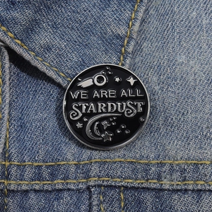 Black enamel pin with We Are All Stardust text on a blue denim jacket lapel