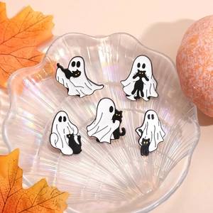 Detail of five cute Halloween ghost and black cat enamel pins in a decorative glass dish