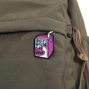 Détail du pin's Silly Goose Juice en émail épinglé sur un sac à dos en toile de couleur verte