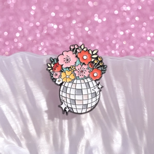 Macro shot of colorful floral enamel disco ball pin on light purple ripple surface