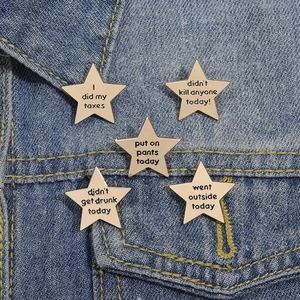 Fünfteiliges goldenes Stern-Emaille-Pin-Set mit Slogans auf blauer Jeansjacke