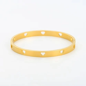 Detalle de cerca de un brazalete de acero de titanio dorado con recortes de corazón