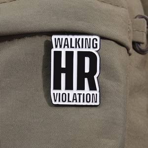 Macro shot of Walking HR Violation enamel pin attached to a green canvas backpack