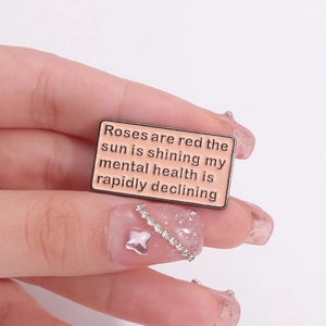 Pink enamel rectangle brooch with funny English text held by fingers on white background