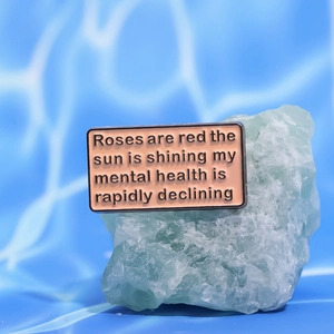 Detail of pink enamel pin with humorous text on green stone against blue water background