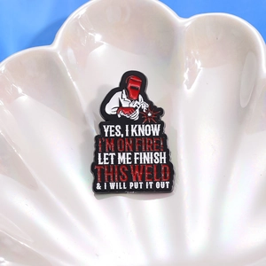 Détail macro du pin's émaillé soudeur avec slogan sur un plateau en forme de coquille