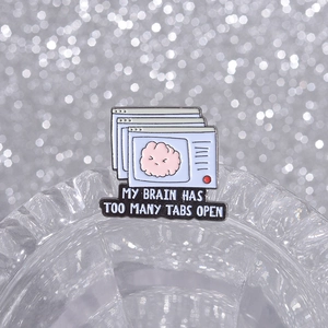 Macro shot of an enamel pin featuring a pink brain and My Brain Has Too Many Tabs Open text