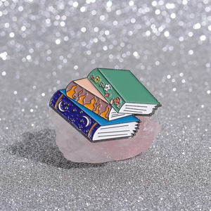 Detailed macro view of stacked magic book enamel pins on pink crystal background