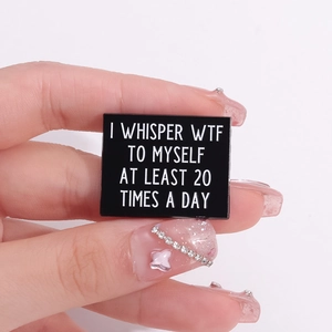 Handheld square enamel pin featuring humorous 'I WHISPER WTF' text on black metal background