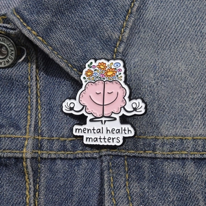 Enamel pin of a meditating pink brain with flowers on denim, mental health matters