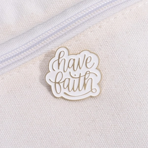 Detailed close-up of a Have Faith enamel pin attached to a white canvas tote bag
