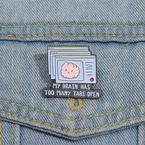 Funny enamel brain pin with My Brain Has Too Many Tabs Open slogan on blue denim jacket