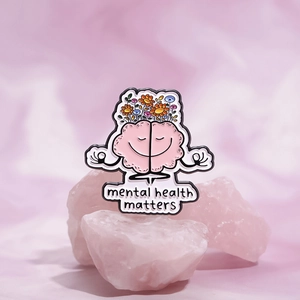 Detail of enamel pin featuring a pink meditating brain with flowers and mental health text