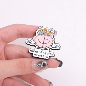 Detail of hand-held enamel pin featuring a meditating brain with flowers and mental health text
