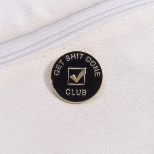 Close-up of a circular black enamel pin featuring GET SHIT DONE CLUB gold text and checkmark