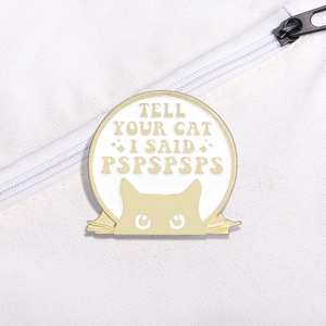 Close-up of a cat enamel pin with Tell Your Cat I Said Pspspsps text on a canvas bag