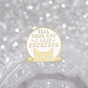 Macro shot of circular enamel cat pin with Tell Your Cat I Said Pspspsps slogan