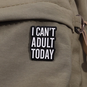 Detailed view of 'I CAN'T ADULT TODAY' enamel pin on a green canvas backpack