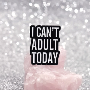 Dettaglio macro della spilla in smalto nero 'I CAN'T ADULT TODAY' con scritte bianche