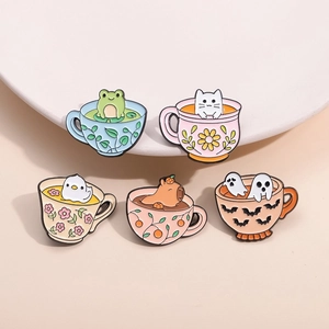 Close-up of five cute enamel pins featuring cartoon animals in teacups and a ghost