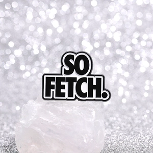 Detail of creative 'SO FETCH!' enamel brooch on white stone with shimmering silver background