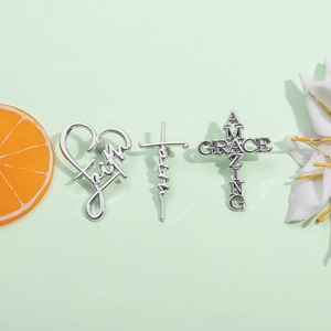 Détail des broches croix et cœur argentées avec texte Faith sur un fond vert naturel
