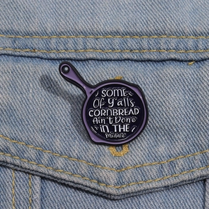 Detailed view of creative frying pan enamel pin on a light blue denim jacket pocket