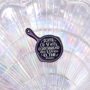 Detailed close-up of a purple enamel frying pan pin with humorous English text engraving