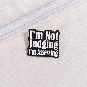Macro d'un pin's en émail I'm Not Judging I'm Assessing sur un sac en toile