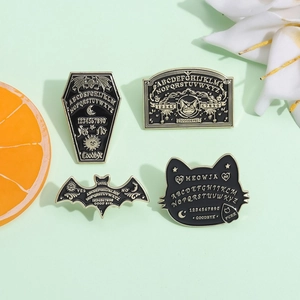 Macro view of four black and gold enamel pins featuring Ouija board and gothic bat motifs