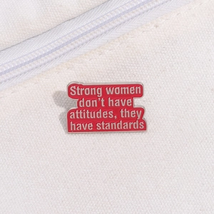 Macro detail of red enamel pin with motivational text and silver wave edge on fabric