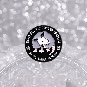 Round enamel opossum pin with humorous text on a silver bokeh background