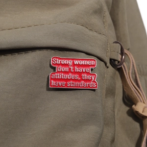 Close-up of inspirational red enamel brooch on green canvas bag with strong women quote