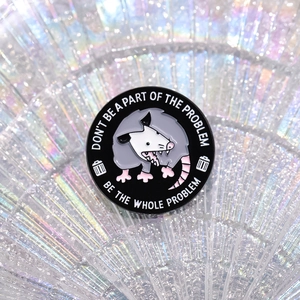 Detailed view of enamel opossum pin with quote on iridescent holographic background