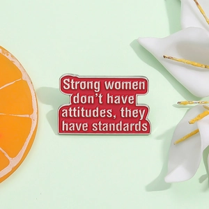 Close-up of red enamel brooch with Strong women don't have attitudes quote
