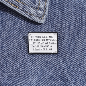 Détail d'un pin's en émail blanc avec texte noir humoristique sur tissu denim bleu
