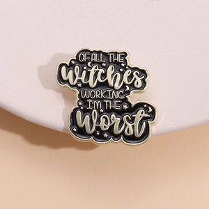 Detail of a black enamel witch brooch with gold accents and creative English typography