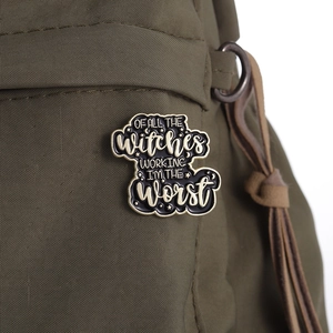 Close-up of black enamel witch brooch with gold lettering on a green canvas bag