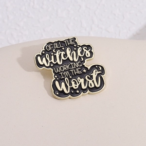 Enamel brooch with 'Witches Working' text in black and gold on beige background