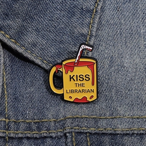 Yellow enamel coffee mug brooch with Kiss The Librarian text on blue denim jacket