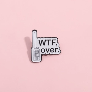 Gros plan d'une épinglette en émail avec talkie-walkie et lettrage 'WTF, over.' sur rose